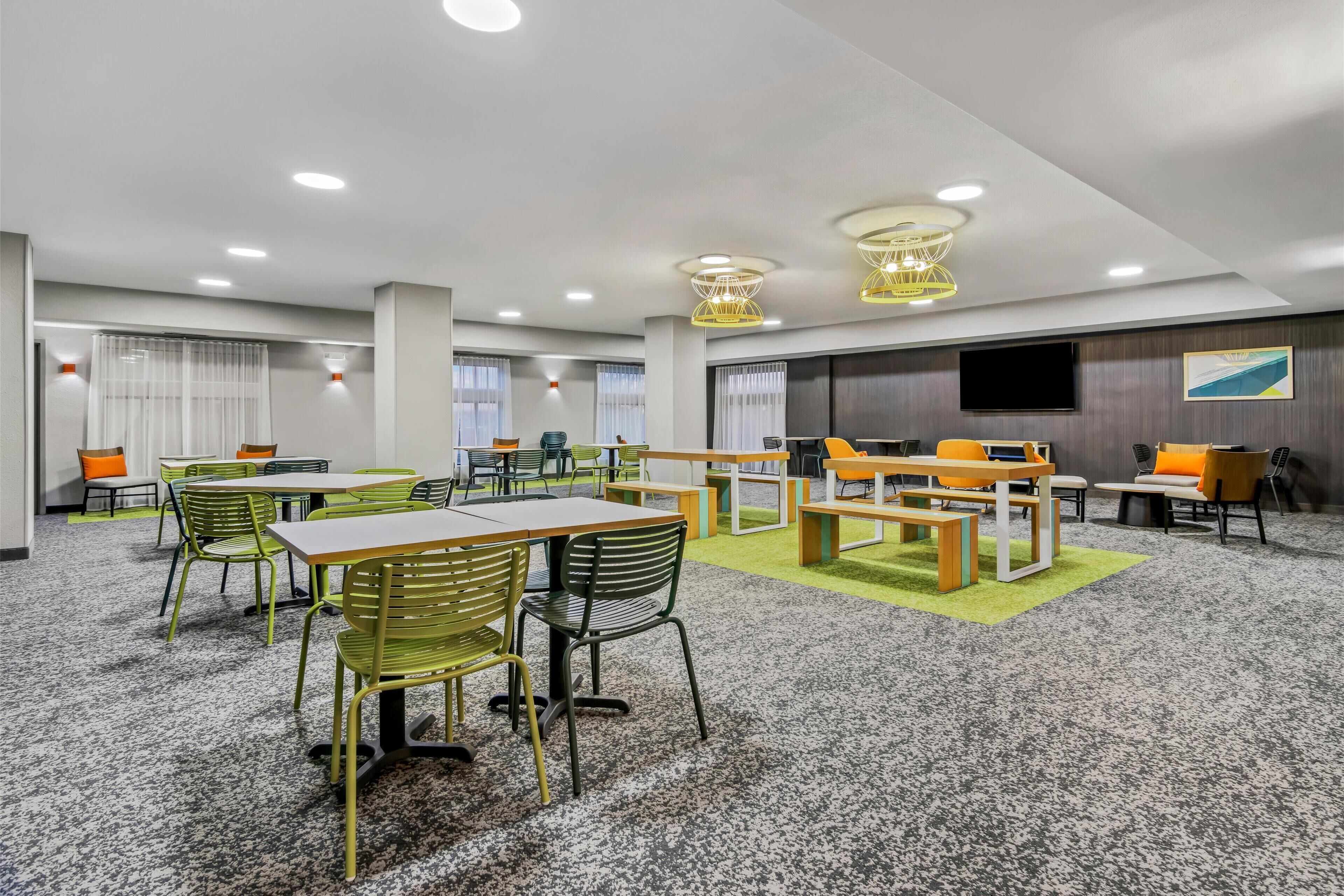 A spacious conference room with multiple tables and chairs, a large flat-screen TV, and a carpeted floor.
