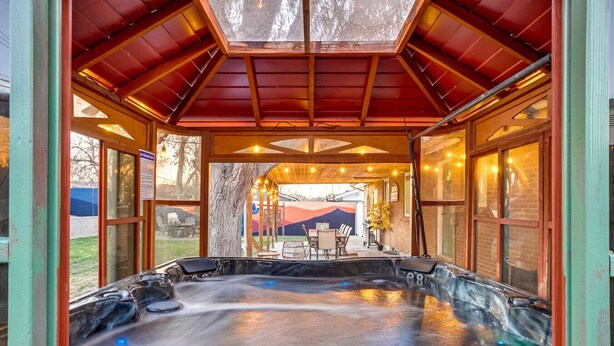 Ein Whirlpoolbereich mit Holzbalkendecke und Glaswänden, umgeben von einer Terrasse mit Sitzgelegenheiten.