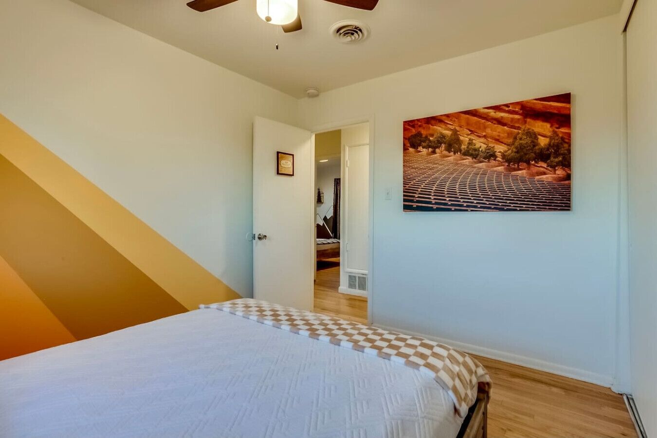 A bedroom with a bed, a painting, and a staircase leading to another room.