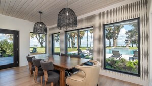 Ein moderner Essbereich mit Holztisch und -stühlen, großen Fenstern mit Blick auf einen Pool und Außenbereich sowie einer Decke aus Holzpaneelen.