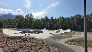 Una pista de skate con varias rampas y una zona de juegos, rodeada de árboles y montañas al fondo.