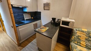Una kitchenette compacta con microondas, cafetera y un lavamanos pequeño.