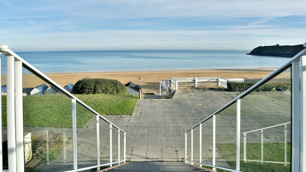 Eine Treppe führt zu einem Strand mit freiem Blick auf das Meer und einer fernen Klippe.