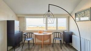 A compact room with a round wooden table, two chairs, a black cabinet, and a large window offering a view of the landscape.