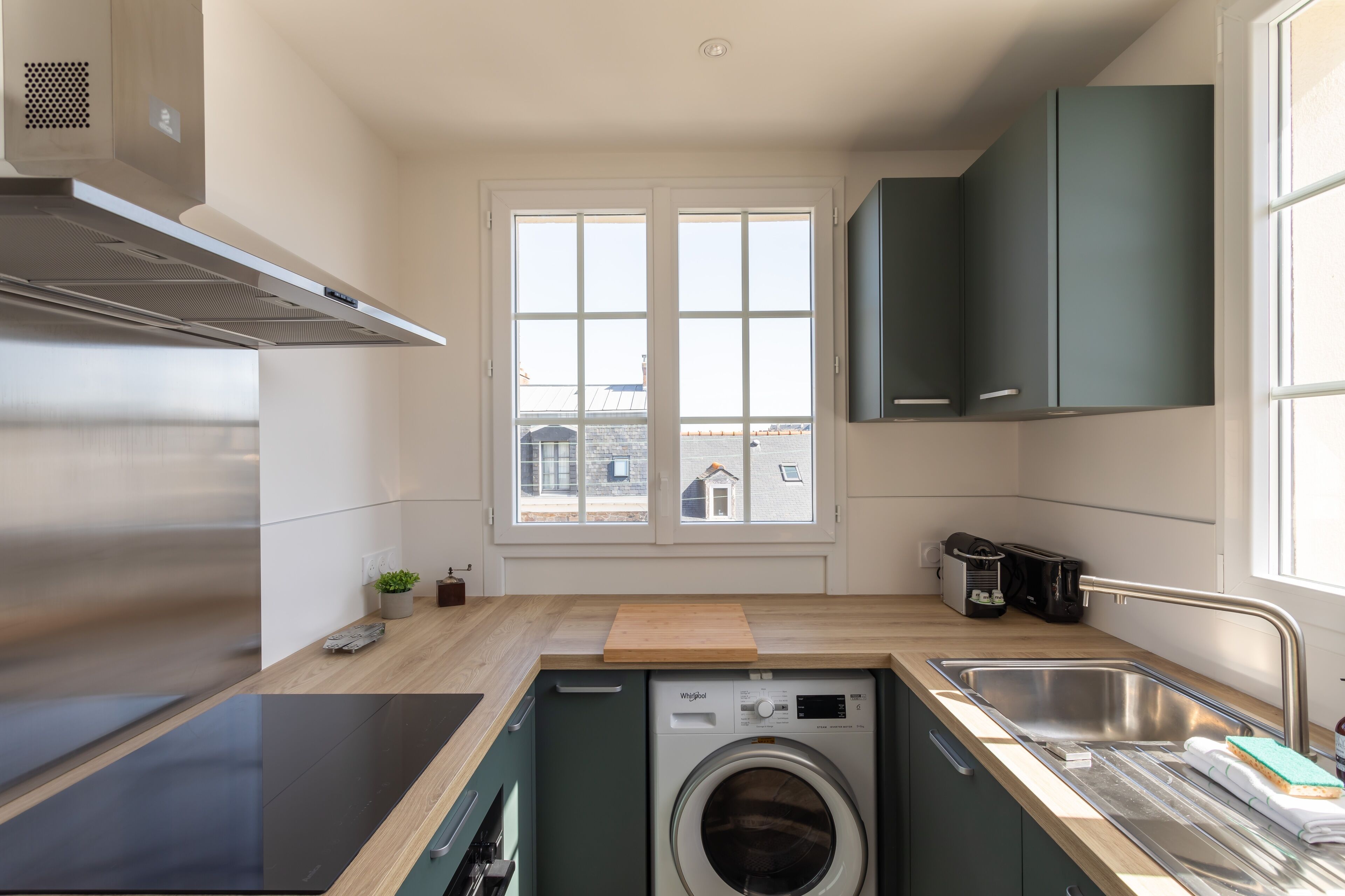 Cocina compacta con lavadora integrada, ventana con vistas a la ciudad y extractor de acero inoxidable.