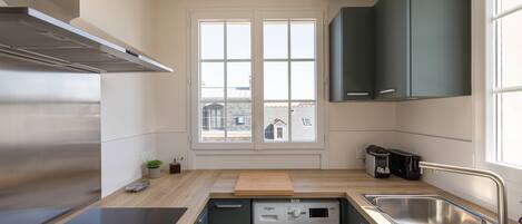 Cocina compacta con lavadora integrada, ventana con vistas a la ciudad y extractor de acero inoxidable.