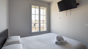 Een hotelkamer met een bed, een aan de muur bevestigde televisie en een raam met uitzicht op gebouwen.