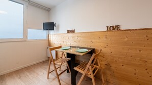 Un petit coin repas avec une table et des chaises en bois, un téléviseur fixé au mur et une fenêtre laissant entrer la lumière naturelle.