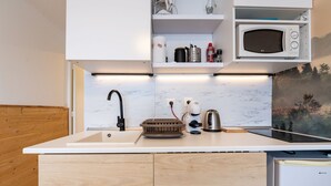 Une cuisine compacte dotée d’un plan de travail blanc, d’un four à micro-ondes encastré, d’une bouilloire et d’un grille-pain.