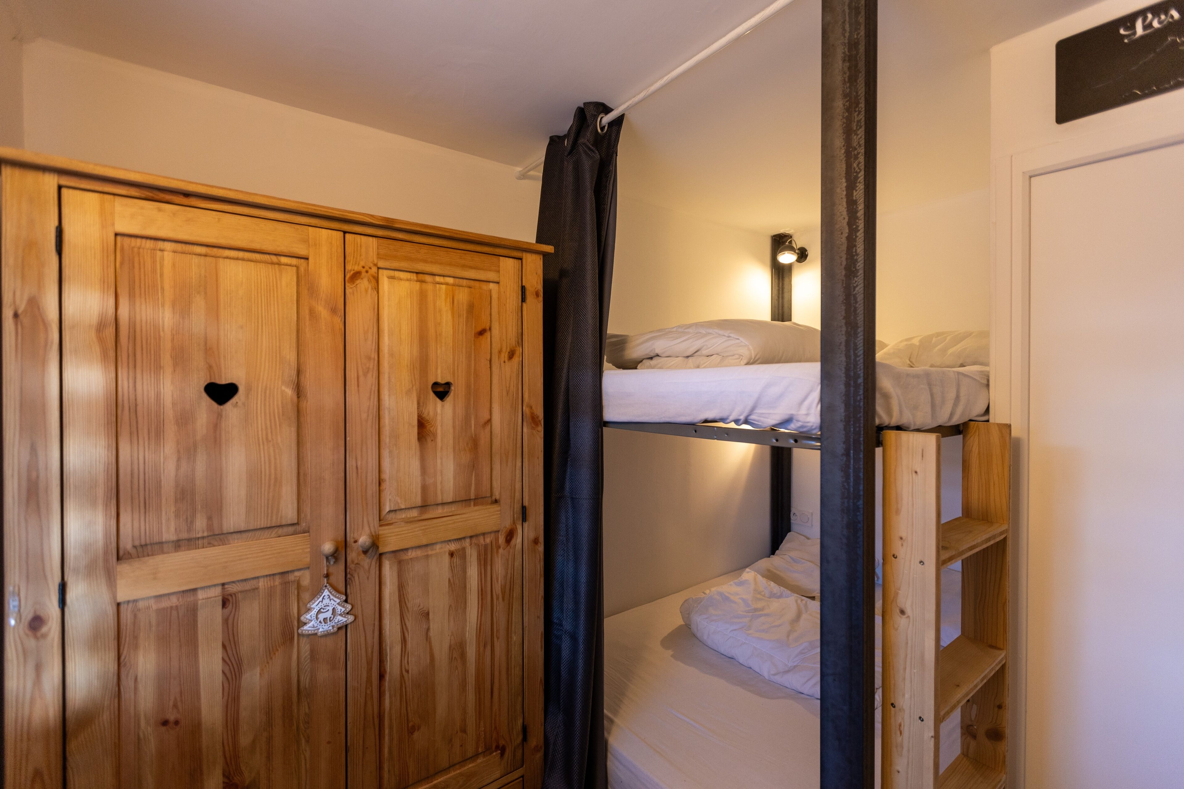 Una habitación con un armario de madera, una cama litera y una pequeña estantería.
