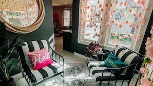 A living room with a sofa, armchair, and a large mirror. There is a window with curtains and a rug on the floor.