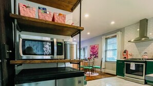 A modern kitchen with stainless steel appliances, a wooden shelf, and a dining area with green chairs.