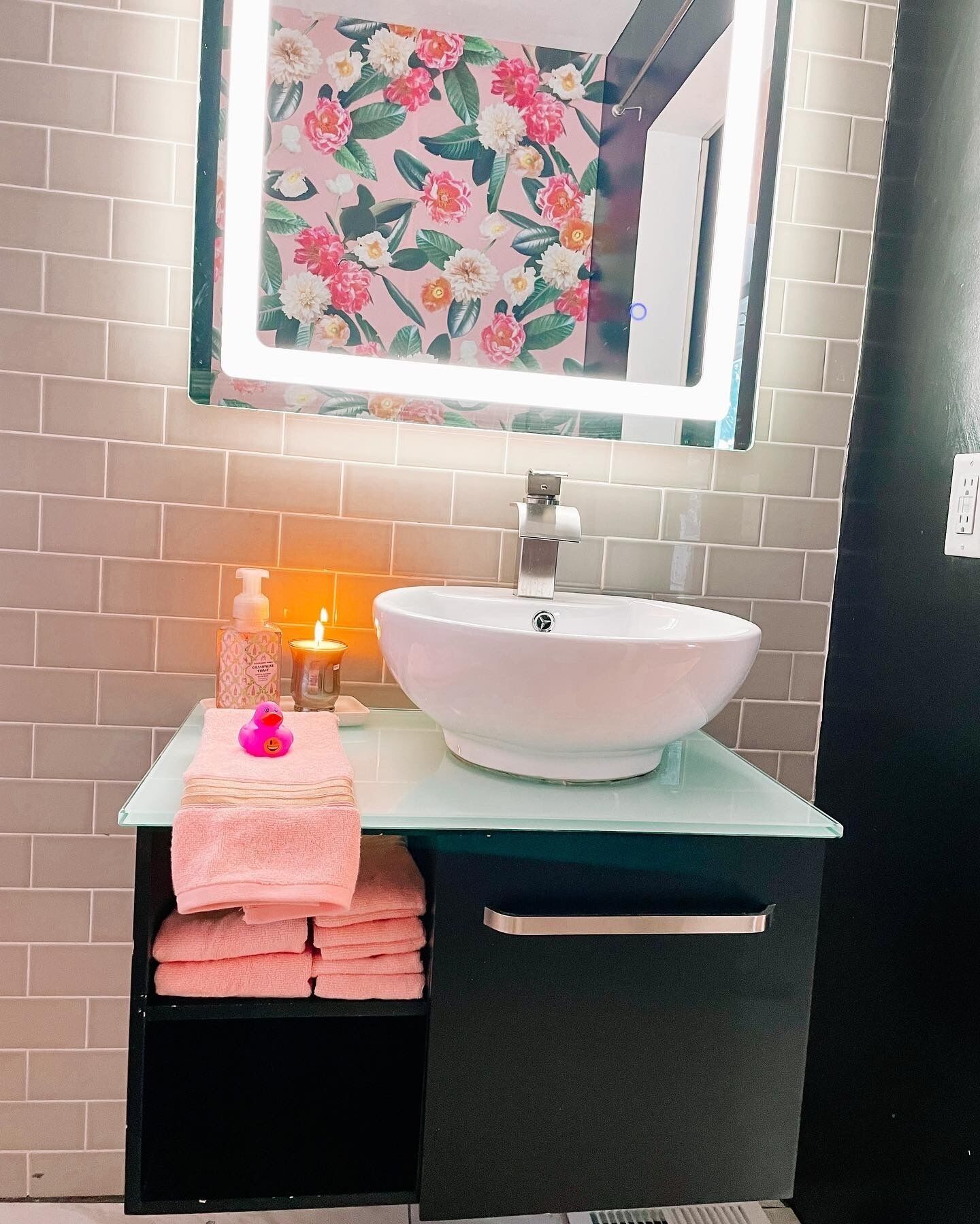 Un baño con un lavabo blanco, un espejo con marco floral y una pila de toallas rosas.