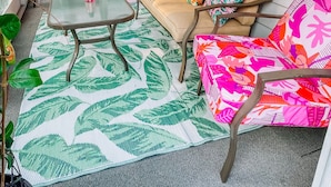 A cozy patio area with a cushioned chair, a small table, and a vibrant patterned rug.