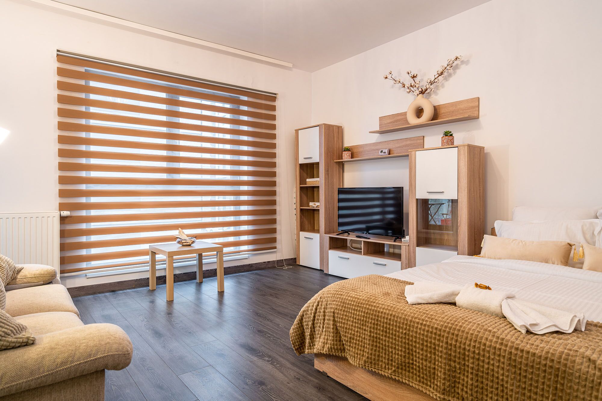 A modern bedroom with a large window, a bed, a TV, and a small table.