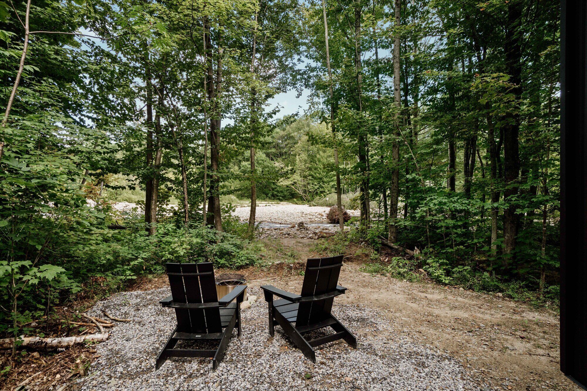 Two Adirondack chairs facing a gravel path leading through a forested area.
