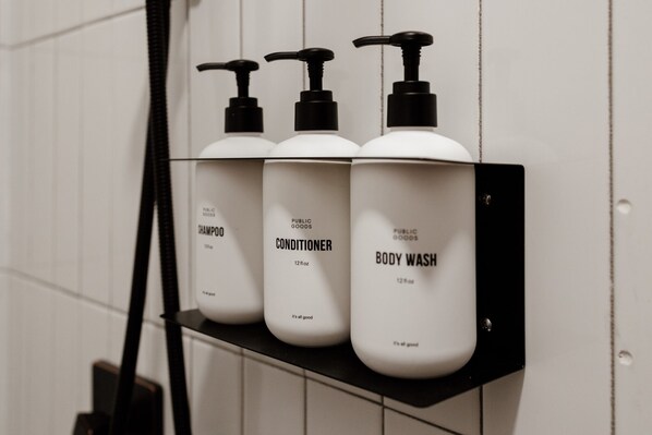 Trois flacons de produits d’hygiène personnelle sont posés sur une étagère noire, devant un mur blanc.