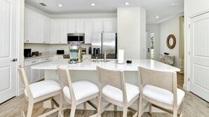 A modern kitchen with white cabinets, a central island with bar stools, and stainless steel appliances.