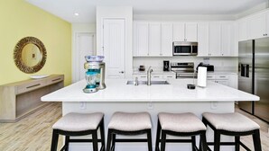 Una cocina moderna con armarios blancos, una isla grande con taburetes de bar, un microondas y un refrigerador de acero inoxidable.