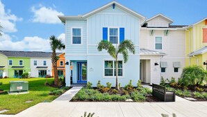 A row of colorful townhouses with a well-maintained lawn and a bench in the front yard. - Lovely Villa near Disney | Margaritaville & Waterpark Access - 2956OR (Kissimmee)