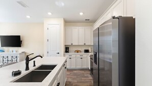 Une cuisine moderne avec des meubles blancs, un réfrigérateur en acier inoxydable et un four encastré.