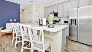 Cocina moderna con muebles blancos, refrigerador de acero inoxidable y una isla integrada con licuadora.