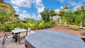 Une terrasse avec une table et des chaises, entourée d’une végétation luxuriante et de palmiers.