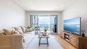 Una sala de estar moderna con un sofá, una mesa de centro, un televisor de pantalla plana y un balcón con vista al mar.