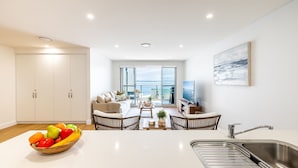 Una cocina moderna con un frutero, un comedor con sillas de mimbre, un televisor y vistas al mar.