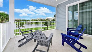 A covered balcony with two Adirondack chairs, a view of a water body, and a building in the background.