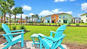 A row of colorful houses with a lawn and two turquoise Adirondack chairs in the foreground.