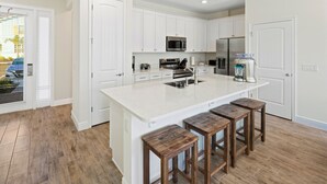 Una cucina moderna con mobili bianchi, una grande isola con sgabelli, elettrodomestici in acciaio inossidabile e pavimento in legno.
