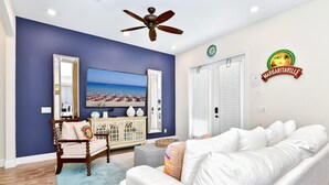 Ein Wohnzimmer mit blauer Akzentwand, Deckenventilator, großem Fernseher und einem Schild mit der Aufschrift 'Margaritaville'.
