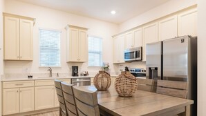 Una cocina moderna con armarios blancos, una mesa de comedor de madera y un refrigerador de acero inoxidable.