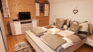 A bedroom with a wooden wall, a bed with a checkered bedspread, a television on a wooden dresser, and a heart-shaped decoration on the wall.