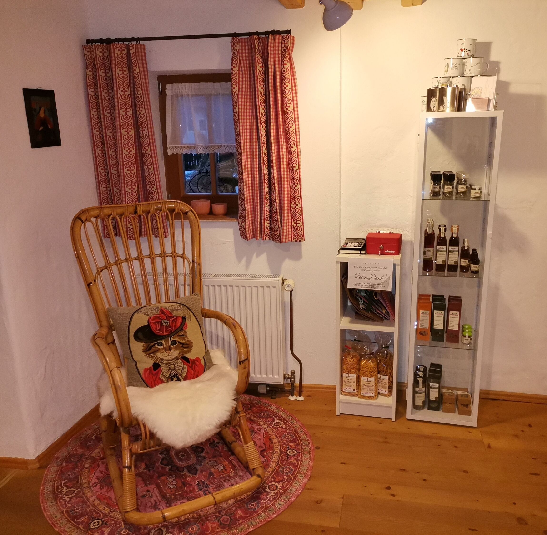 Una habitación con una silla de mimbre con cojín, un radiador, un estante con botellas y una ventana con cortinas.