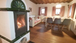 A cozy living room with a fireplace, a sofa, a dining table with chairs, and a wooden ceiling.