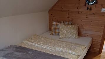 Un lit avec une literie à motifs, un plaid gris et une tête de lit en bois, dans une pièce dont le sol est recouvert de parquet.
