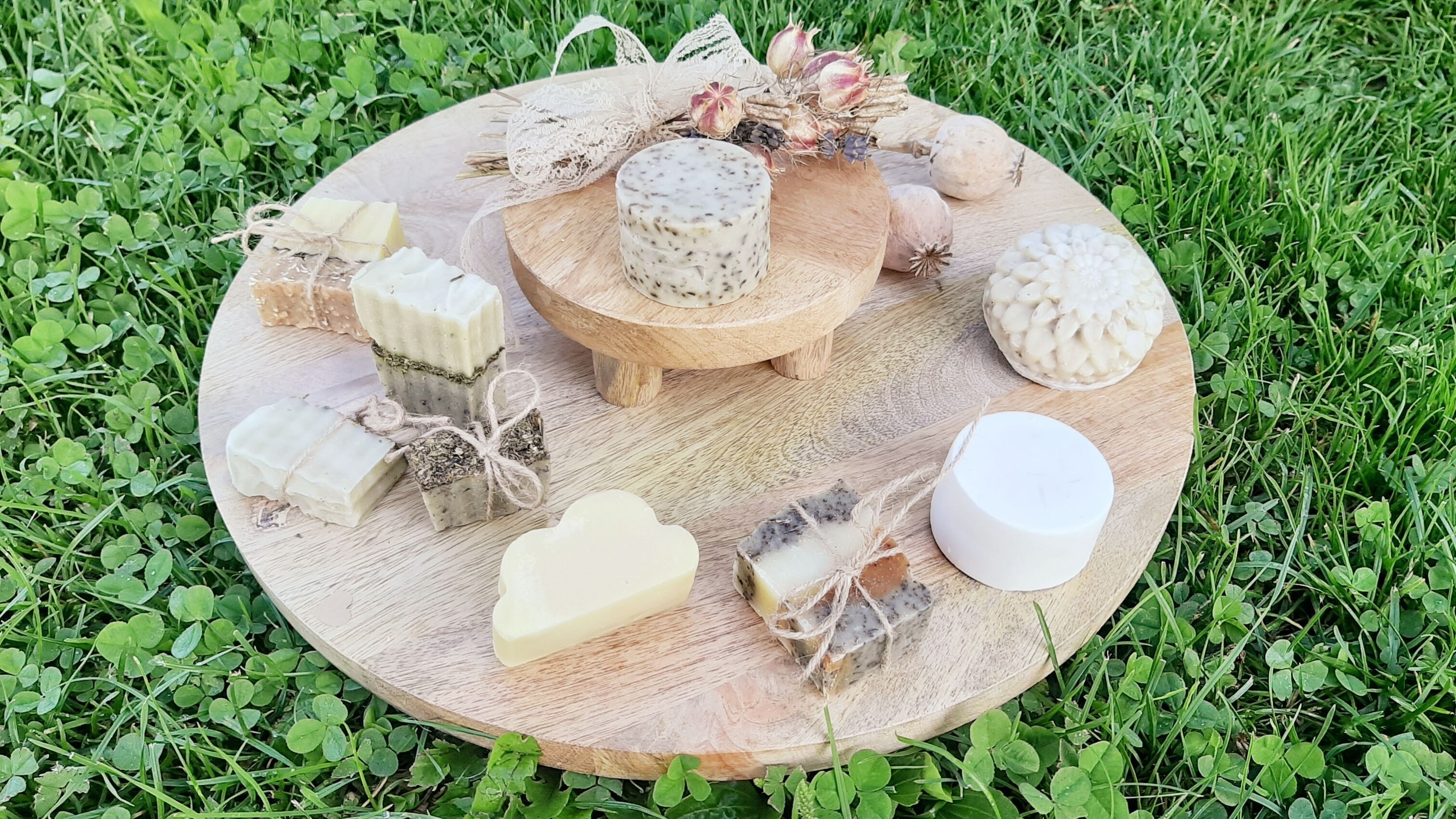 Une planche en bois sur laquelle sont disposés différents fromages, ainsi qu’un petit fromage rond, présenté sur un présentoir, le tout entouré de verdure.