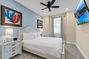 A hotel room with a bed, a nightstand, a lamp, a ceiling fan, and artwork on the walls.