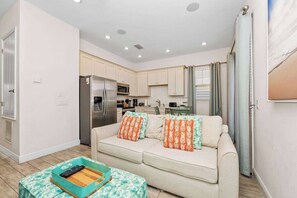 A compact living space with a kitchenette, a sofa with patterned cushions, and a small table with a remote control.