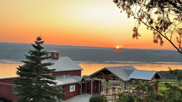 A lodge with a covered patio and a view of the sunset over a lake. - VRFLX Seneca View Bungalow | Hot Tub Retreat (Burdett)