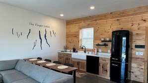 Eine moderne Küche mit Holzvertäfelung, einem schwarzen Kühlschrank und einem Essbereich mit grauem Sofa und Platzdeckchen.