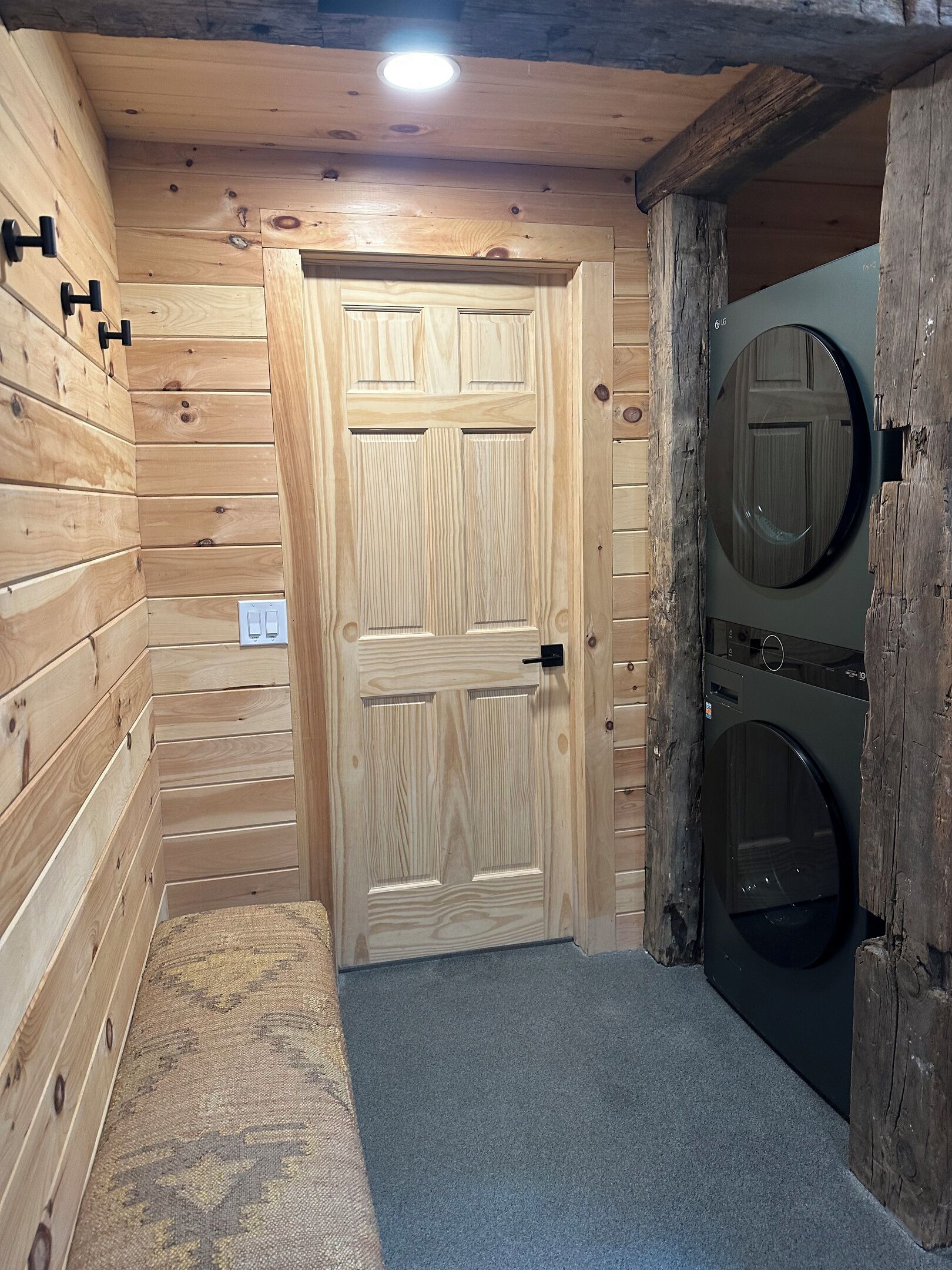 Interior de madeira com uma porta, máquina de lavar e luminária.