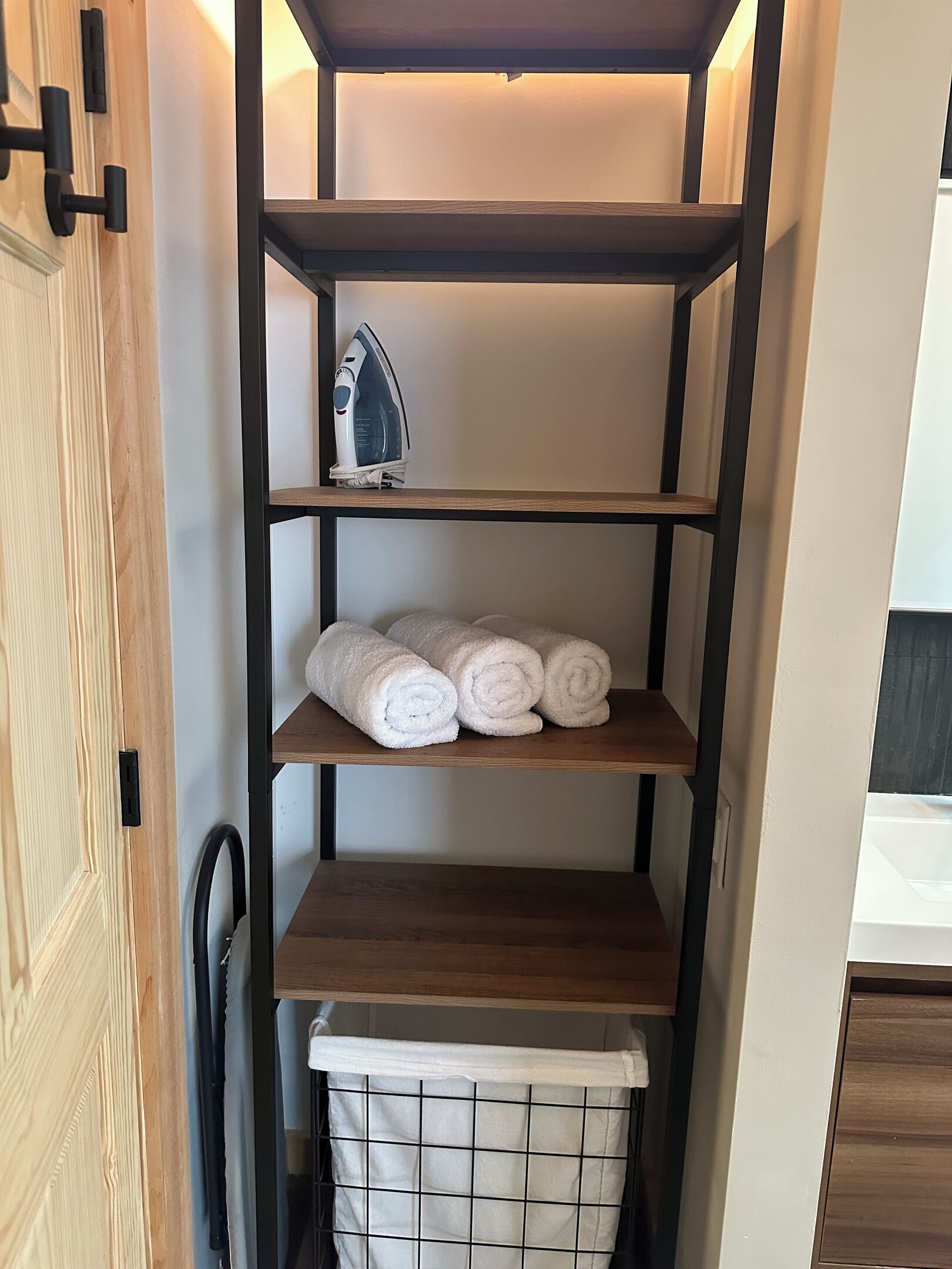 Une étagère en bois avec un panier à linge suspendu et un fer à repasser posé sur l’étagère supérieure.