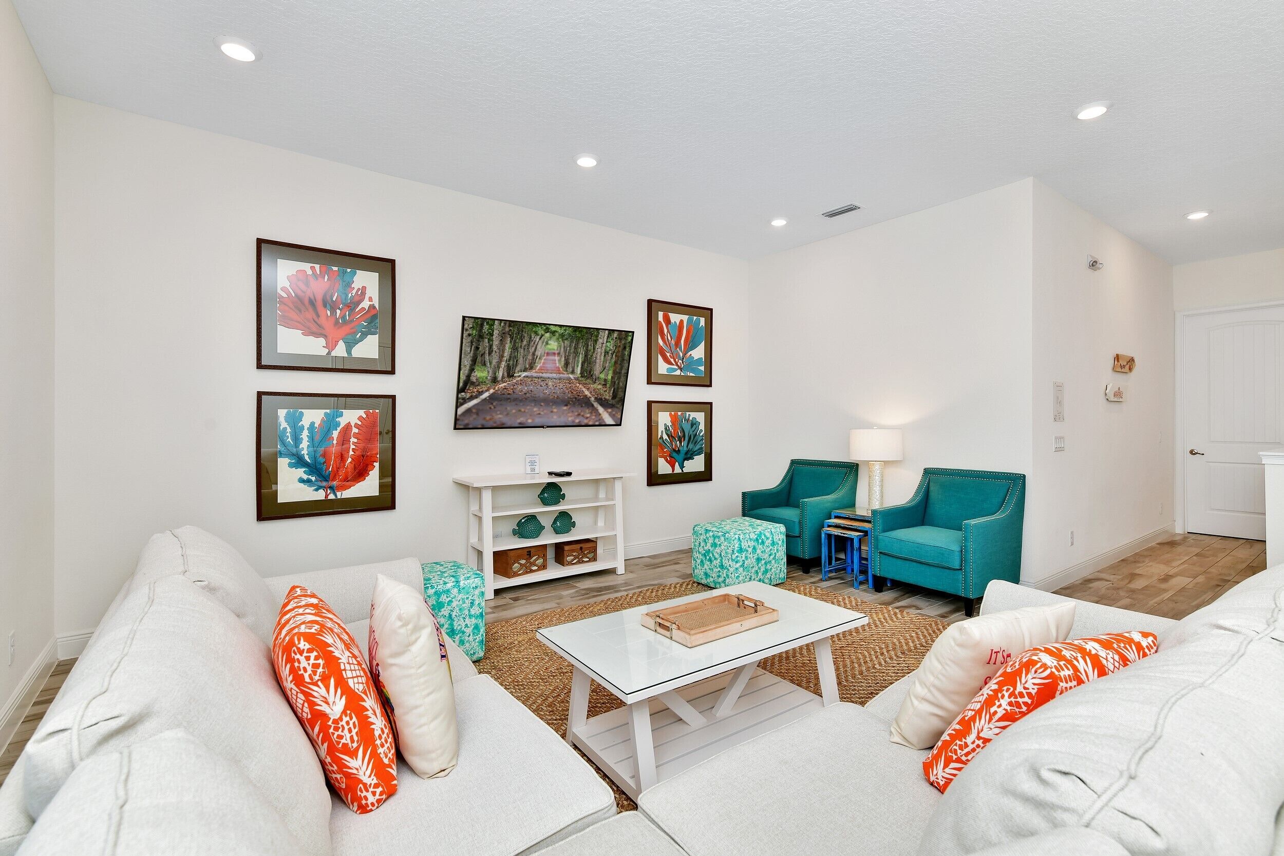 A living room with a white sofa, teal armchairs, a coffee table, and framed artwork on the walls.