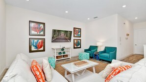 A living room with a white sofa, teal armchairs, a coffee table, and framed artwork on the walls. - Pink Cottage near Disney | Margaritaville Resort & Waterpark Access - 8141SU (Kissimmee)