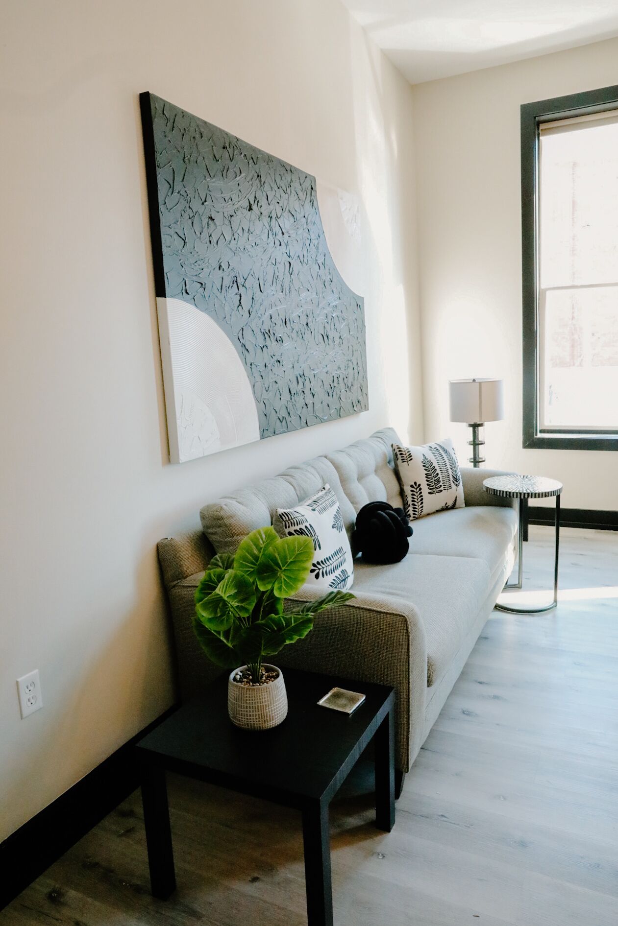 A modern living room with a sofa, a coffee table, a potted plant, and a side table.
