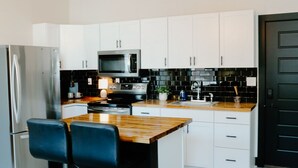 A modern kitchen with white cabinets, a wooden island with bar stools, stainless steel appliances, and a chandelier.