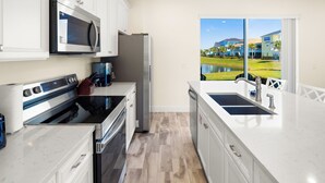 Cocina moderna con armarios blancos, electrodomésticos de acero inoxidable y un amplio ventanal con vistas a una zona residencial.